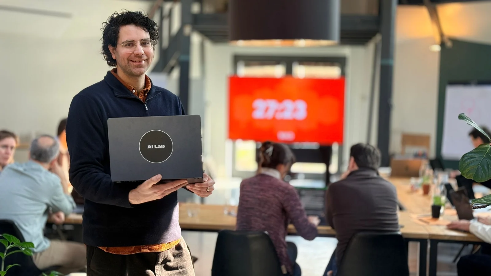 Facilitator holding an AI Lab laptop with workshop participants working together behind him
